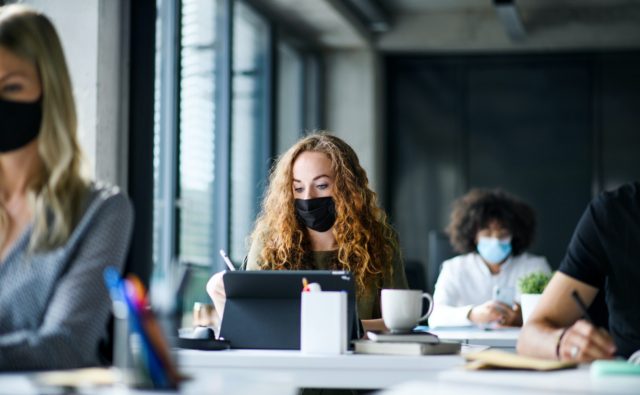 Young people with face masks back at work or school in office after lockdown